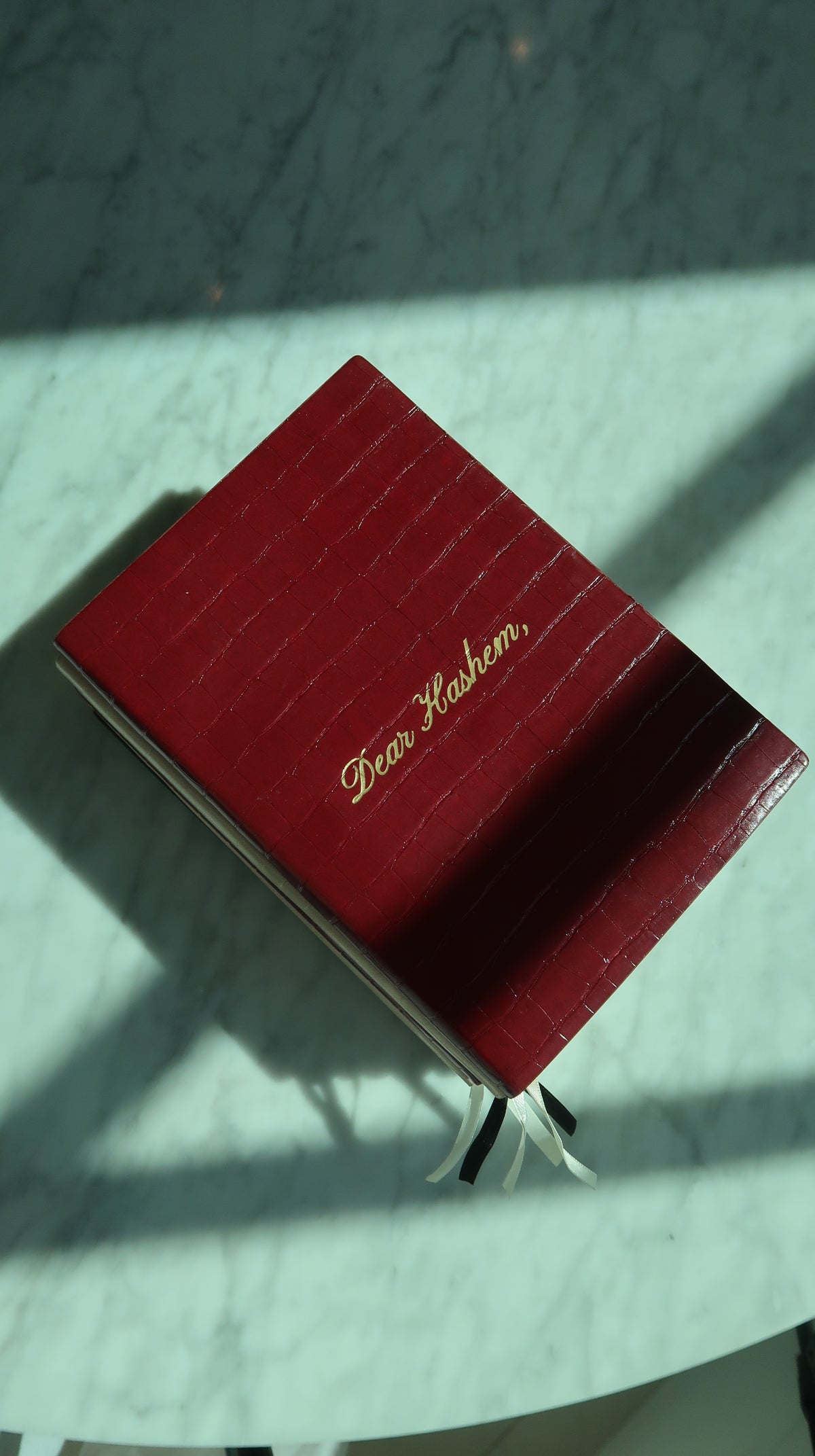 Cherry Dear Hashem Journal with gold lettering, photographed on a sunlit stone table